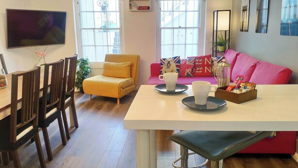 En moderne stue med spiseplads, med en sofa, stole, et bord og kunst på væggene.