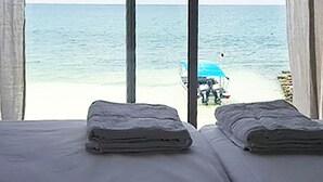 Een kamer met twee bedden, uitzicht op het strand en een blauwe parasol in de verte.