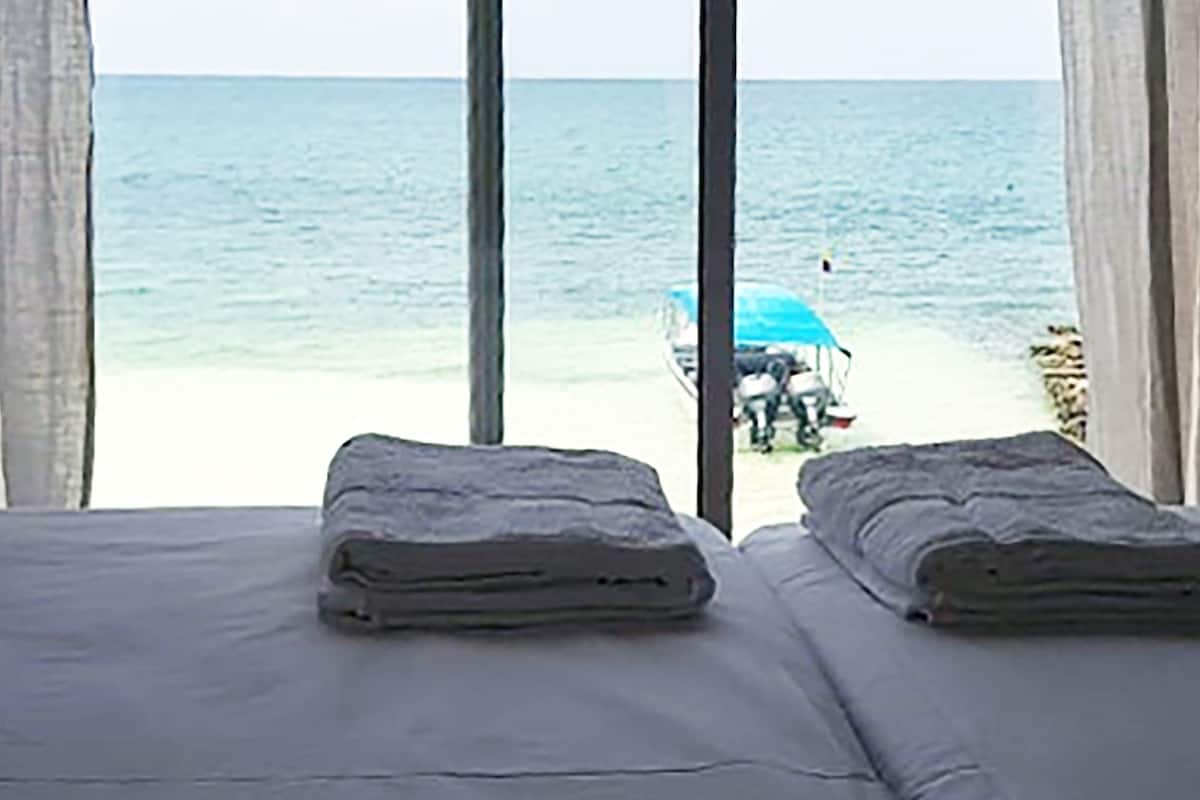 Una habitación con dos camas, vista a la playa y un paraguas azul a lo lejos.