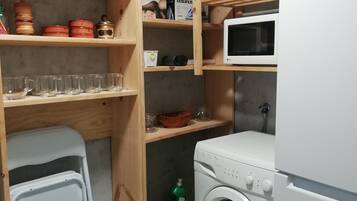 A laundry room with a washing machine, shelves with kitchenware, and a microwave.