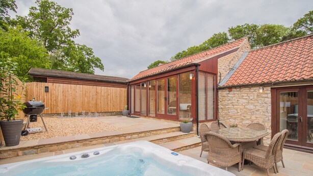 A backyard with a hot tub, a barbecue grill, wicker furniture, and a stone wall.