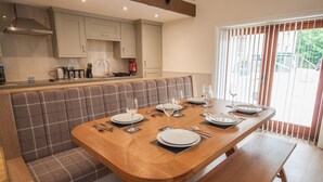 A dining area with a wooden table set for four, a bench seating area, and a kitchen in the background.