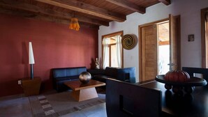 Un salon chaleureux avec un plafond en bois, un mur rouge, un canapé noir, une table basse ornée d’une sphère décorative et une citrouille posée sur une table.