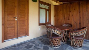 Une façade en bois, une terrasse en pierre, une porte en bois et une fenêtre avec des rideaux.