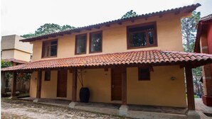 Un bâtiment à deux étages, doté d’un toit recouvert de tuiles, d’un porche abrité et d’une entrée pavée de pierres.