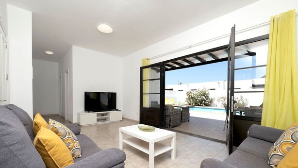 A modern living room with grey sofas, a white coffee table, and a flat-screen TV. - Villa Dulce Vista - 3 bedrooms, Heated Private Pool, with Mountain Views (Playa Blanca)