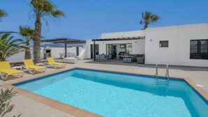 A modern pool area with a clear blue pool, yellow lounge chairs, and a covered seating area with tables and chairs. - Villa Dulce Vista - 3 bedrooms, Heated Private Pool, with Mountain Views (Playa Blanca)
