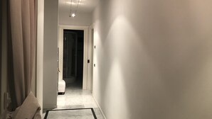Een hal met een marmeren vloer, een witte deur aan het einde en een lamp aan het plafond.