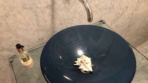 Een badkamer met een glazen wastafel, een handzeepfles en een decoratieve schelp.