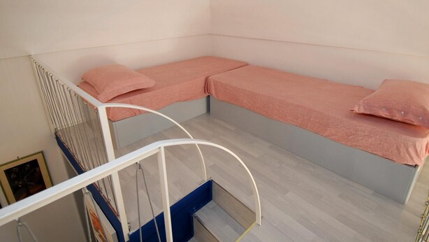 Une chambre d’angle avec deux lits simples, un escalier en métal blanc et un tableau encadré au mur.