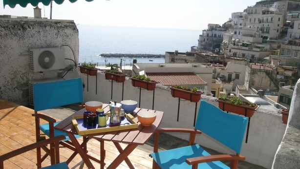 Une terrasse avec une table et des chaises, offrant une vue sur le paysage urbain de la côte, avec ses bâtiments et la mer.