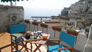 Une terrasse avec une table et des chaises, offrant une vue sur le paysage urbain de la côte, avec ses bâtiments et la mer.