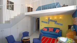 Un vaste espace de vie comprenant un canapé bleu, deux fauteuils bleus, un tapis à rayures rouges et une table blanche sur laquelle est posé un vase décoratif.