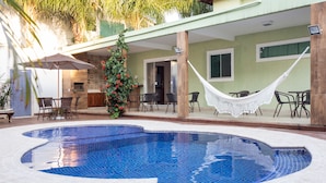 Una piscina con borde de azulejos, rodeada por un patio con mobiliario exterior y una hamaca.