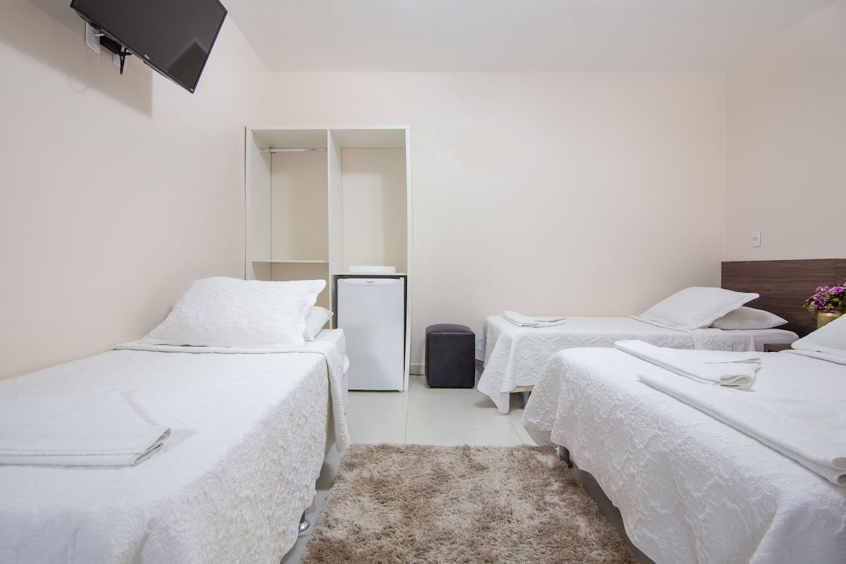 Une chambre d’hôtel avec deux lits simples, un petit réfrigérateur, un miroir et un téléviseur fixé au mur.