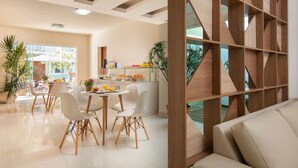 Una cocina moderna con armarios blancos, una zona de comedor con sillas blancas y un separador de madera.
