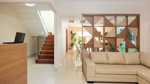 Una sala de estar moderna con un sofá beige, un mostrador de recepción de madera y una escalera que lleva a un piso superior.