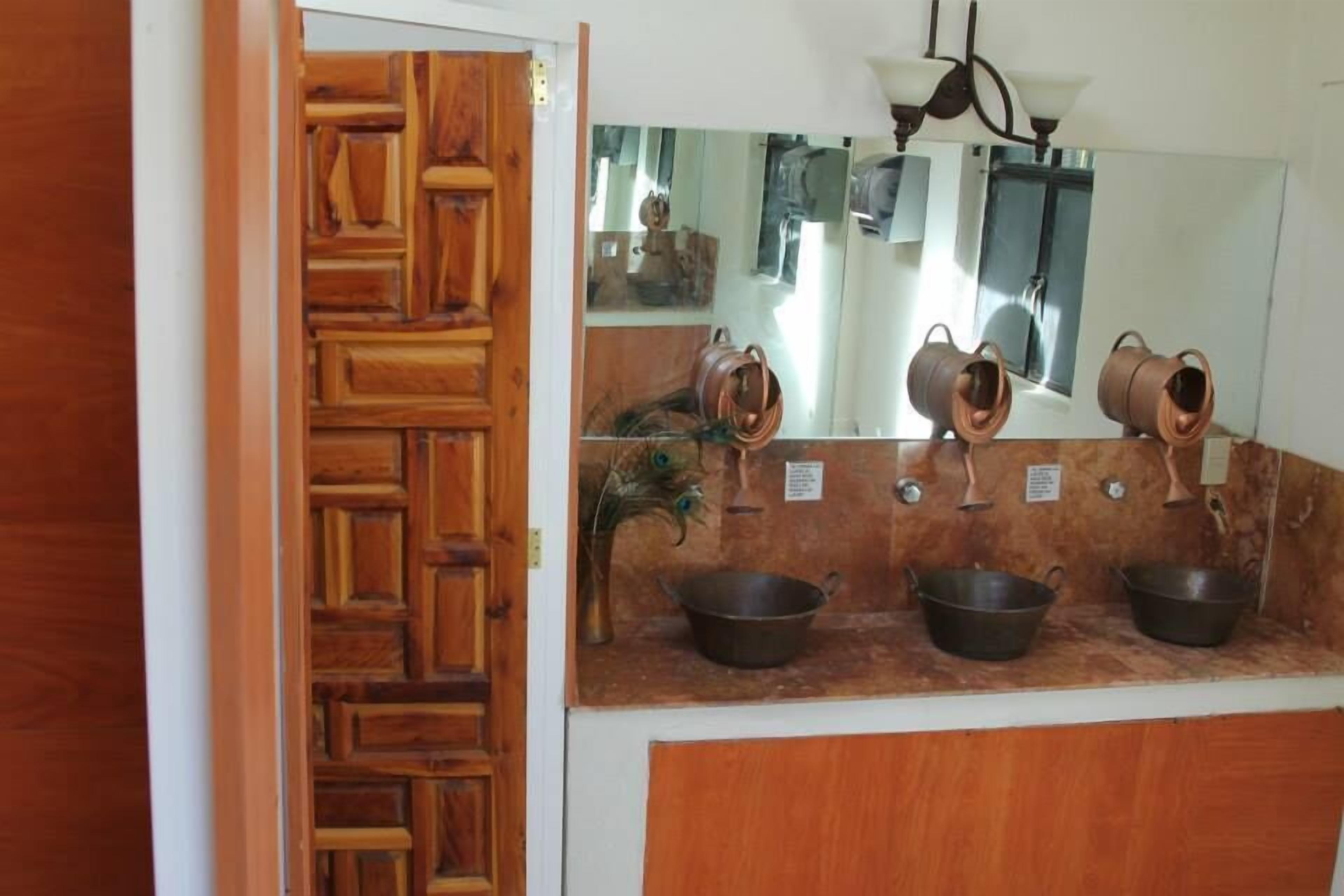 Une salle de bain avec une porte en bois, un miroir et trois casseroles en cuivre posées sur le comptoir.