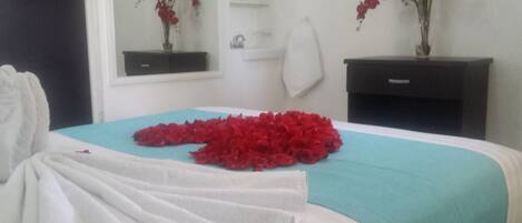 Une chambre d’hôtel avec un lit recouvert d’une couverture bleue, un peignoir blanc posé sur le lit et un bouquet de fleurs rouges sur la table de chevet.