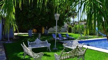 A pool area with white wrought iron benches, a pool, and a palm tree.