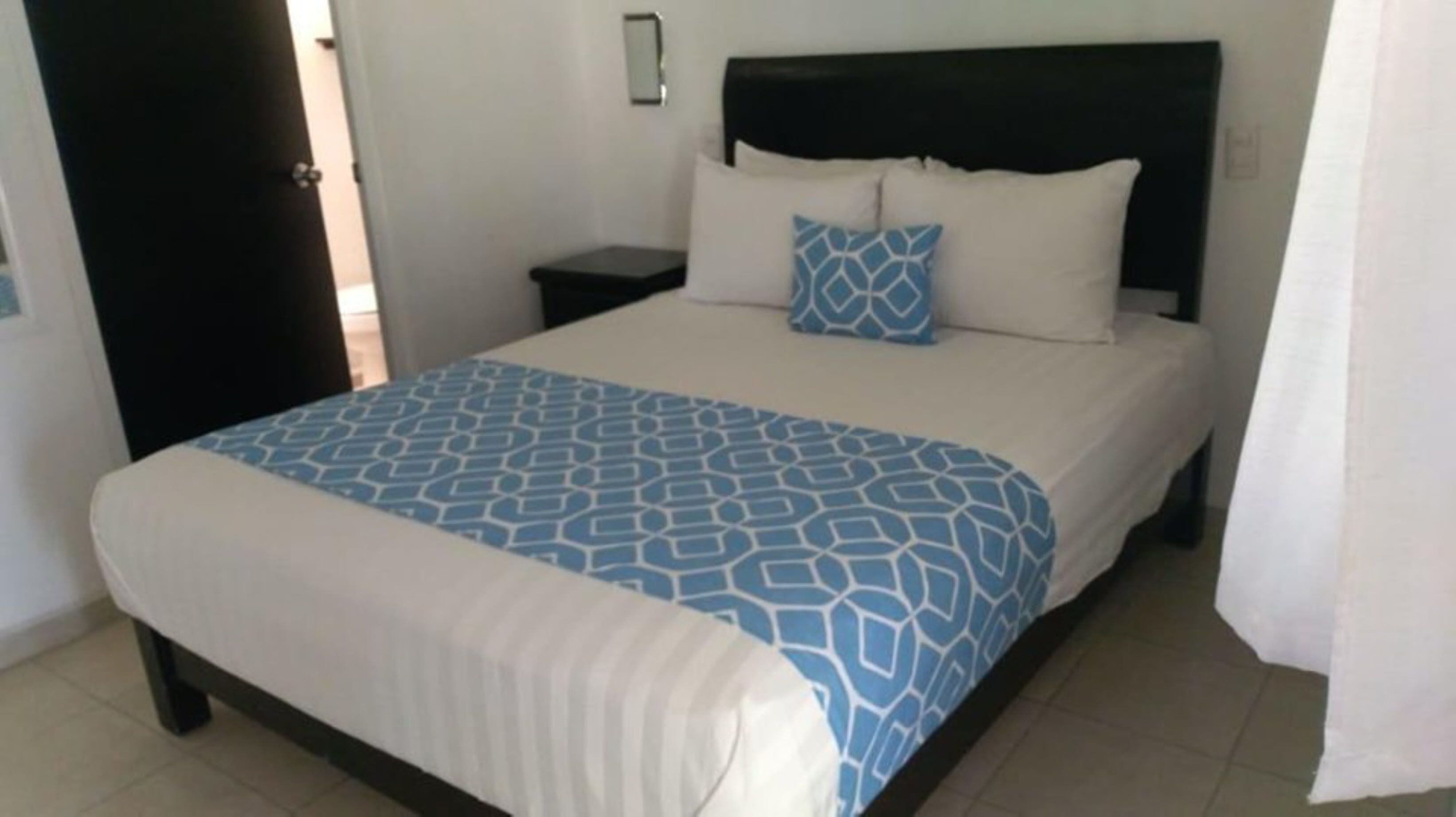 A neatly made bed with a patterned bedspread, a black headboard, and a bedside table with a lamp.