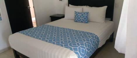 A neatly made bed with a patterned bedspread, a black headboard, and a bedside table with a lamp.