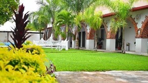 Um pátio com gramado bem cuidado, móveis decorativos brancos e palmeiras.