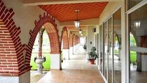 Um corredor coberto com arcos de tijolo e piso de azulejos, que leva a uma área com portas de vidro.