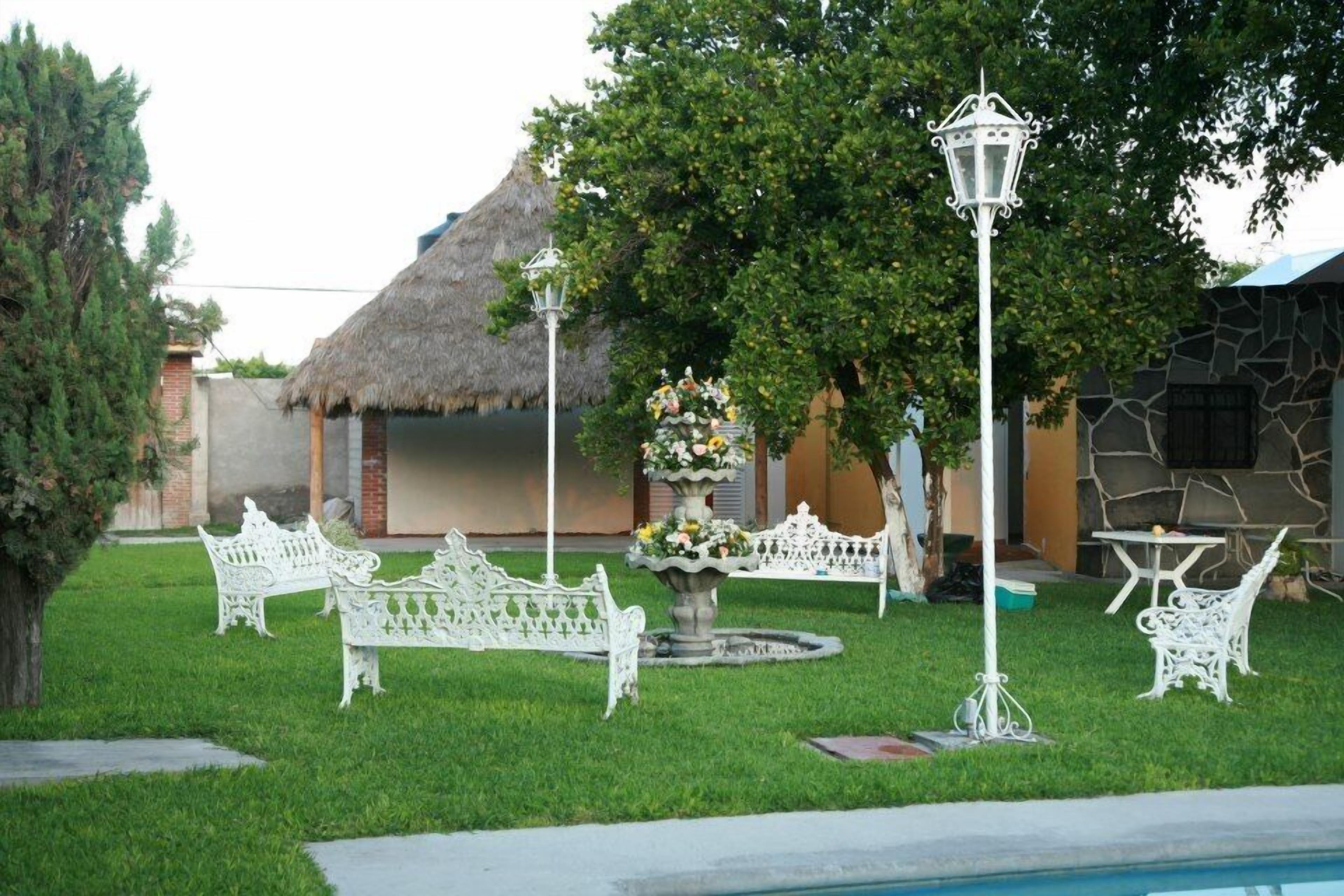 A well-maintained outdoor area with a thatched-roof structure, white metal furniture, and a central decorative fountain.