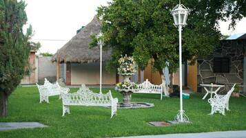A well-maintained outdoor area with a thatched-roof structure, white metal furniture, and a central decorative fountain.