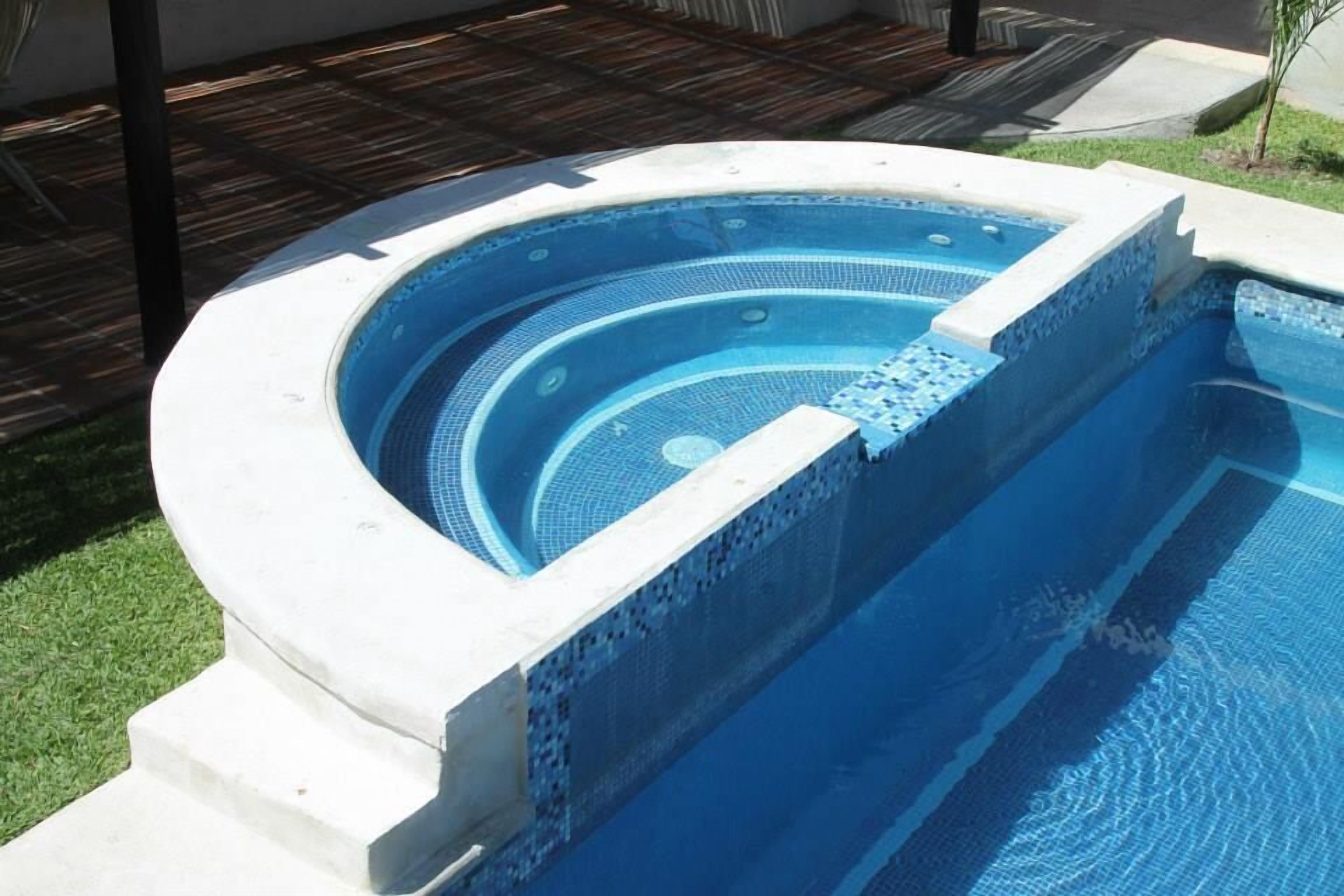 A hot tub with a tiled interior, surrounded by a concrete deck and a grassy area.