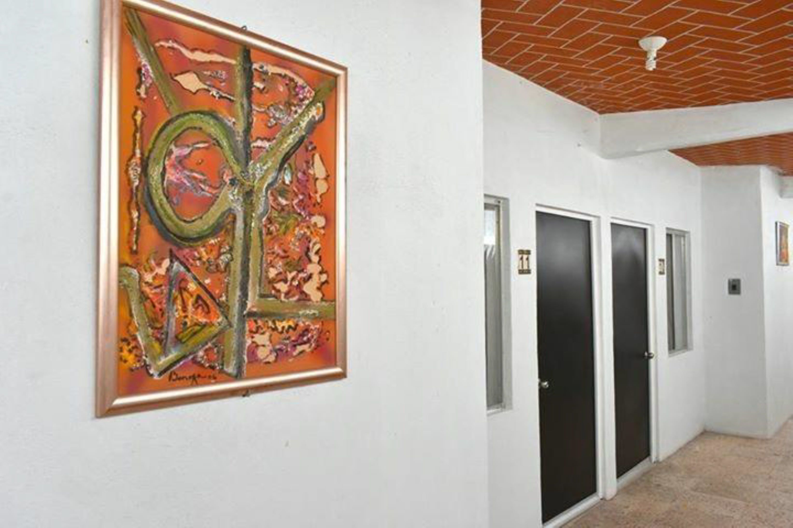 A hallway with a large abstract painting on the wall, a tiled floor, and a ceiling with exposed brickwork.