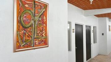 A hallway with a large abstract painting on the wall, a tiled floor, and a ceiling with exposed brickwork.