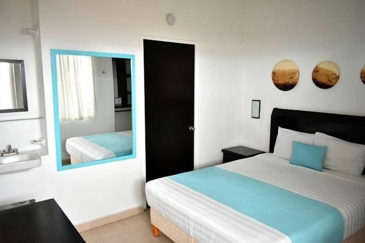 A hotel room with a bed, a nightstand, a mirror, a door, and a wall-mounted circular decoration.