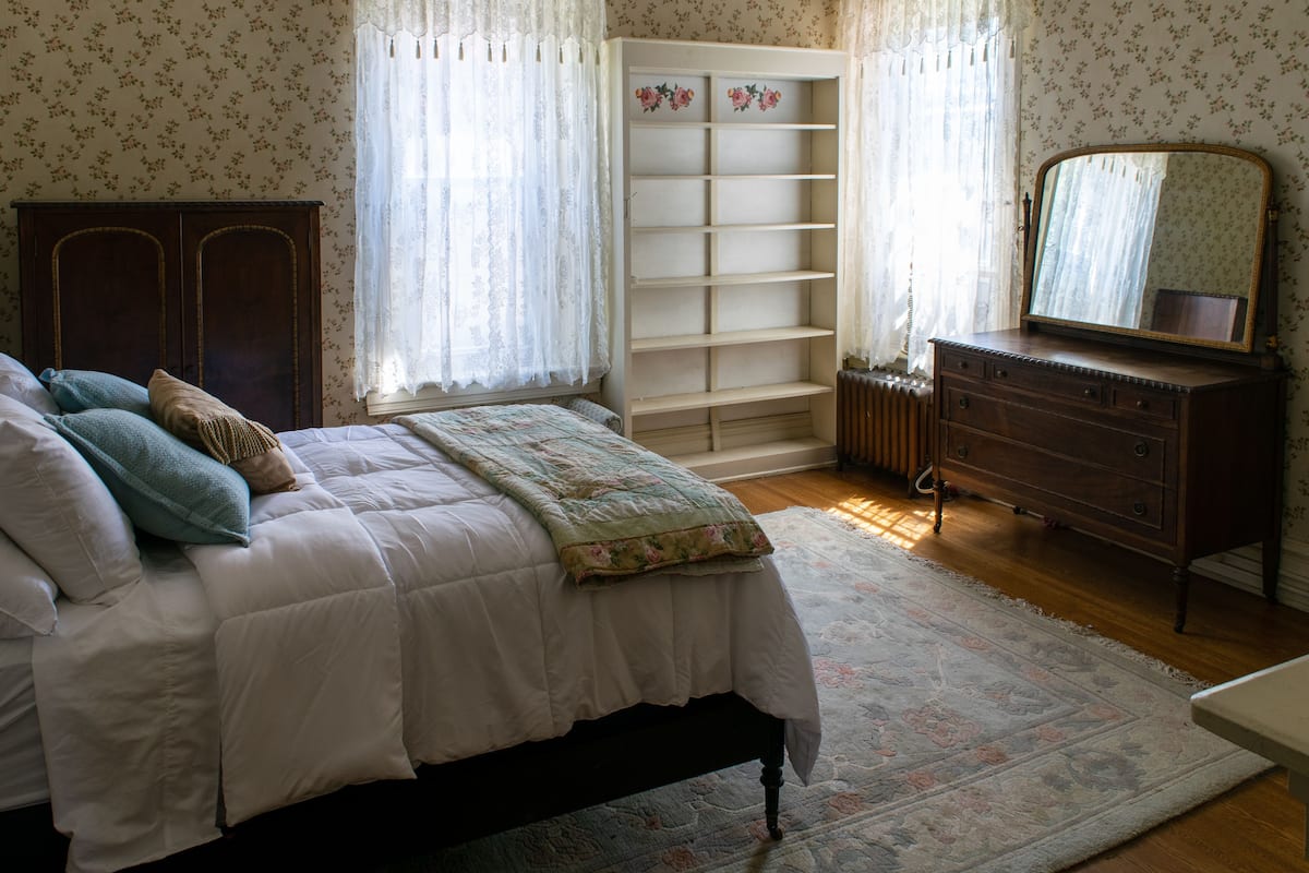 A bedroom with a bed, dresser, mirror, and built-in shelving unit.