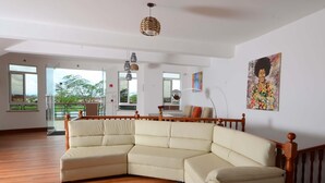 Un salón amplio con un sofá modular en forma de L, piso de madera y un balcón con barandilla.
