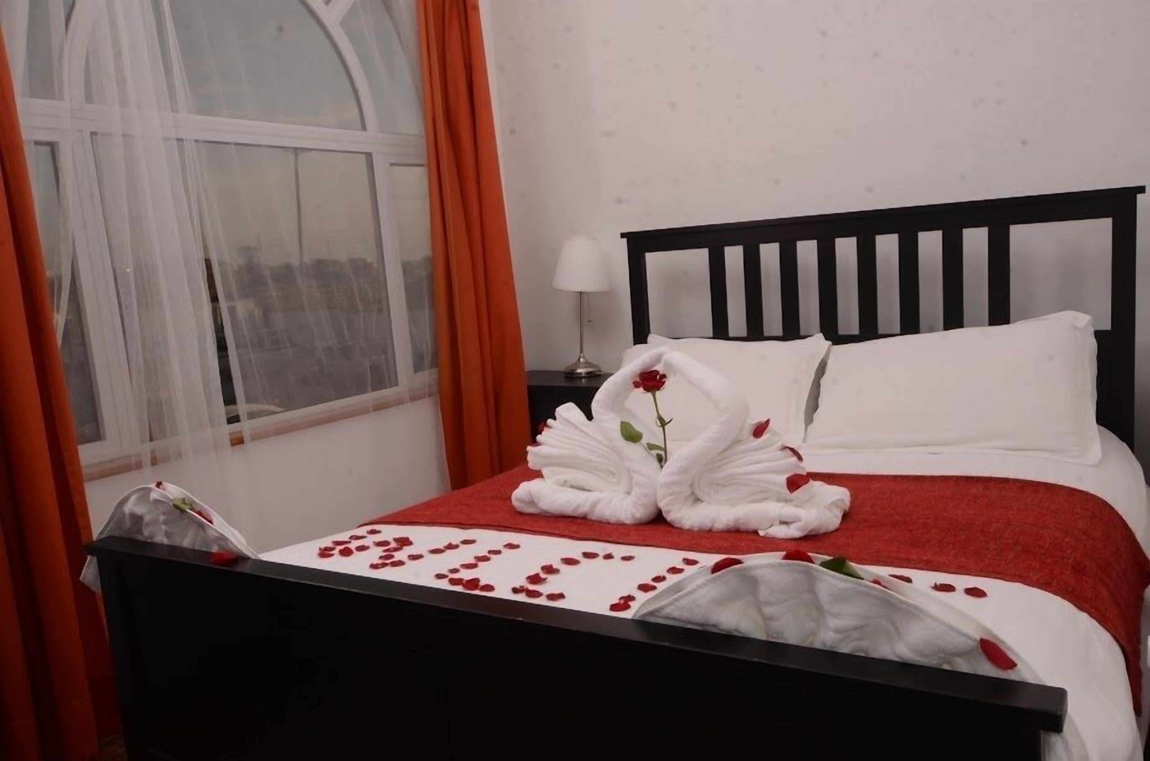 A neatly made bed with a red and white bedspread, a white pillow, and a decorative rose arrangement on the bed.