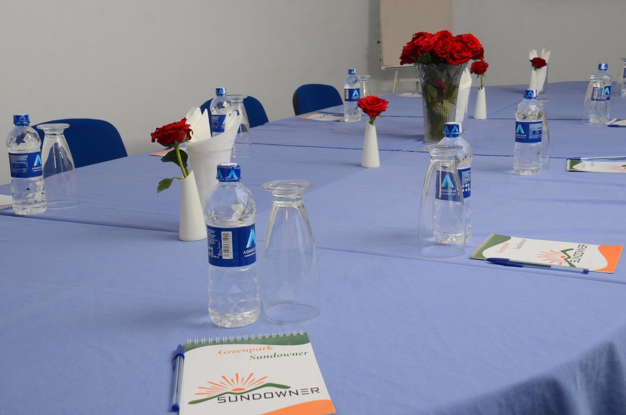 A conference table with water bottles, vases with red roses, and a notebook labeled "Greenpark Sunowner".