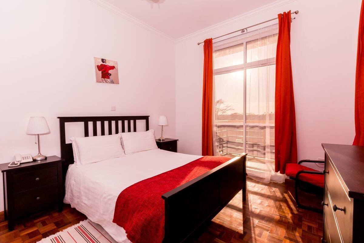 Un dormitorio con una cama, mesitas de noche, un escritorio y un ventanal con cortinas.