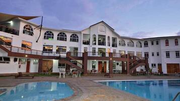 Un hotel de varios pisos con piscina, mobiliario exterior y una escalera que conecta los niveles.