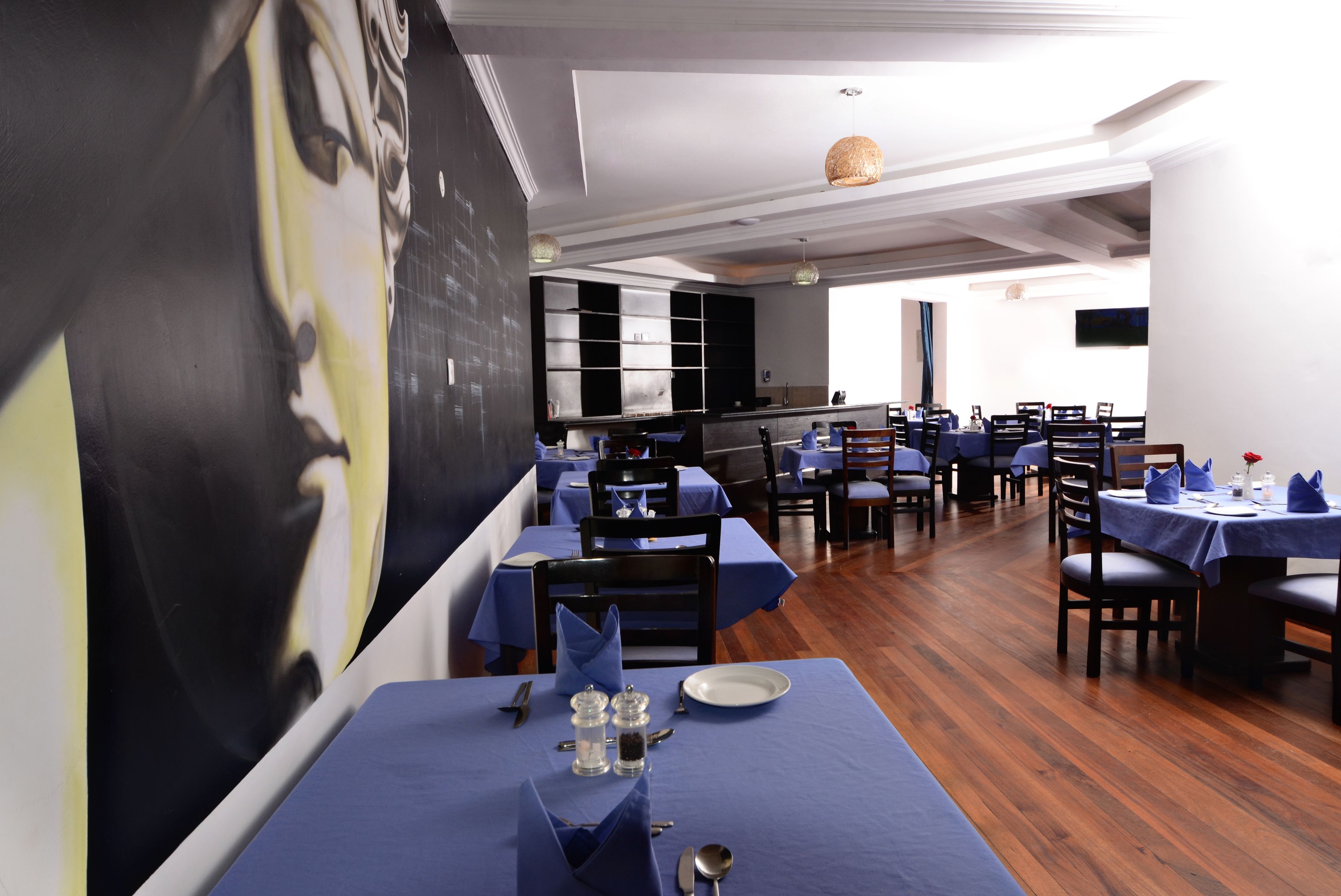 A restaurant with tables set for dining, a large mural on the wall, and a kitchen area in the background.