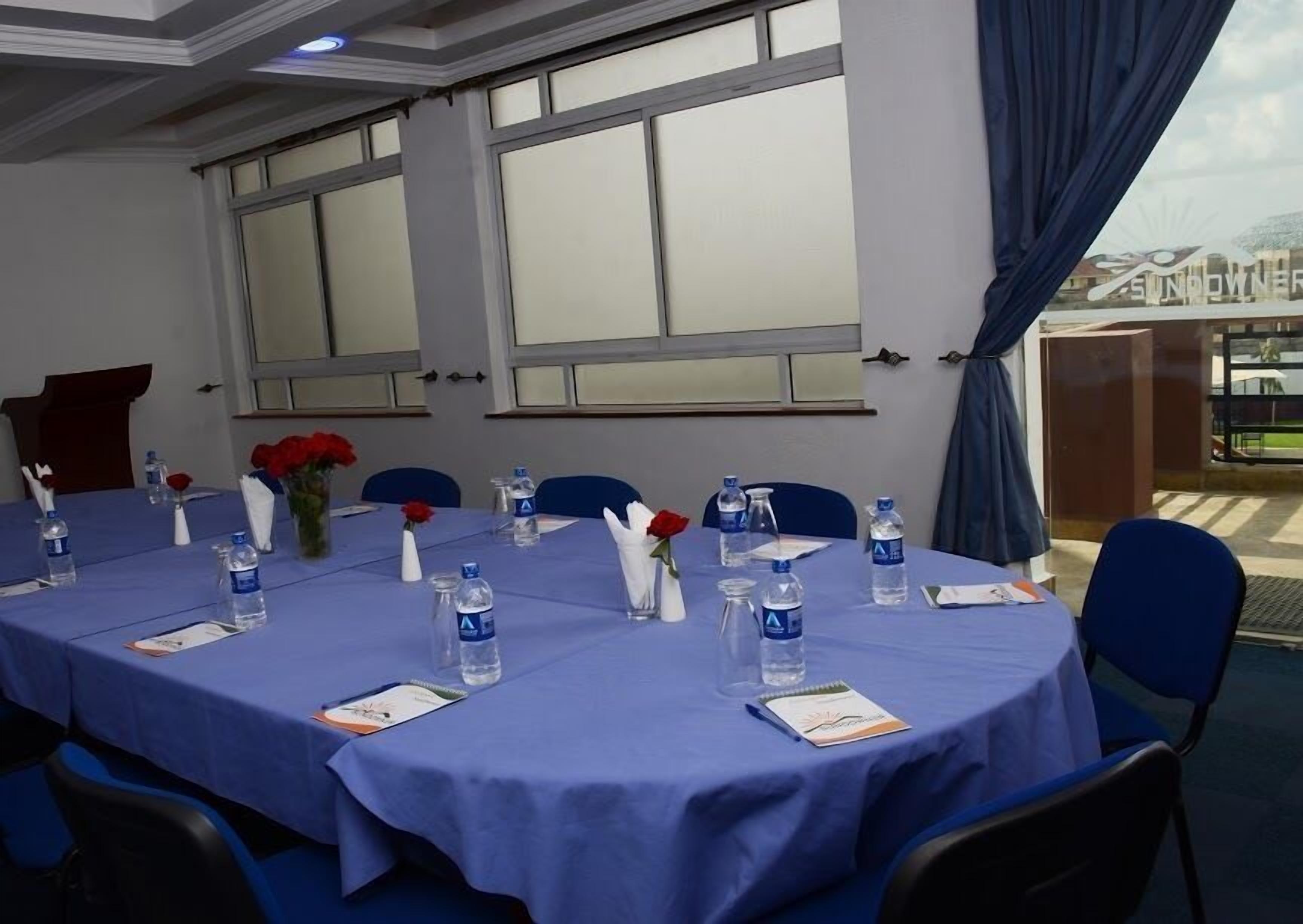 Un salón de conferencias con mantel azul, botellas de agua y rosas rojas sobre la mesa.