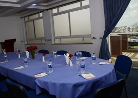 Un salón de conferencias con mantel azul, botellas de agua y rosas rojas sobre la mesa.