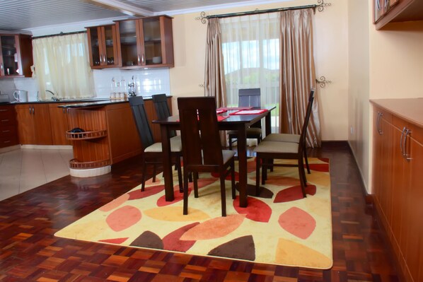 A dining area with a wooden table and chairs, a kitchen with wooden cabinets, and a patterned rug on the floor.