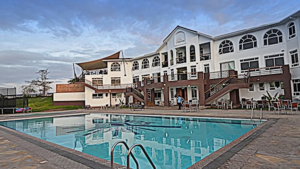 Un hotel con piscina, mobiliario exterior y un edificio grande con múltiples ventanas y balcones.