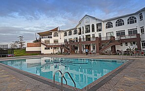 A hotel with a swimming pool, outdoor seating, and a large building with multiple windows and balconies.