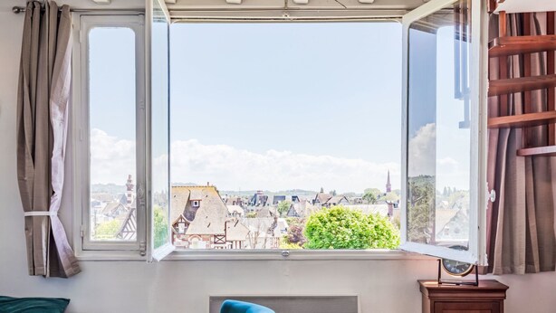 Ein Zimmer mit einem großen Fenster, einem blauen Stuhl, einem Tisch mit kariertem Tischläufer und einem Heizkörper.