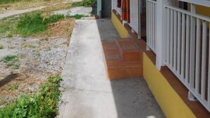 A yellow building with a covered porch, a concrete pathway, and a view of the ocean.