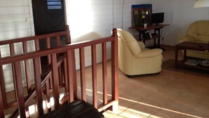 A living room with a wooden staircase, a beige sofa, a yellow armchair, a television, and a painting on the wall.
