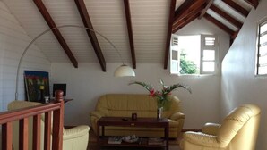 A living room with a sofa, armchair, and coffee table. There is a painting on the wall and a window with a view of greenery.